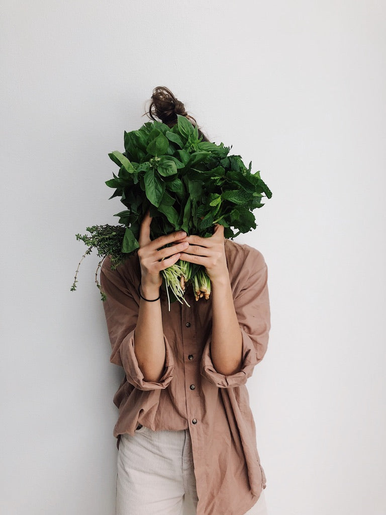 A lady holding over her face a bunch of salad green