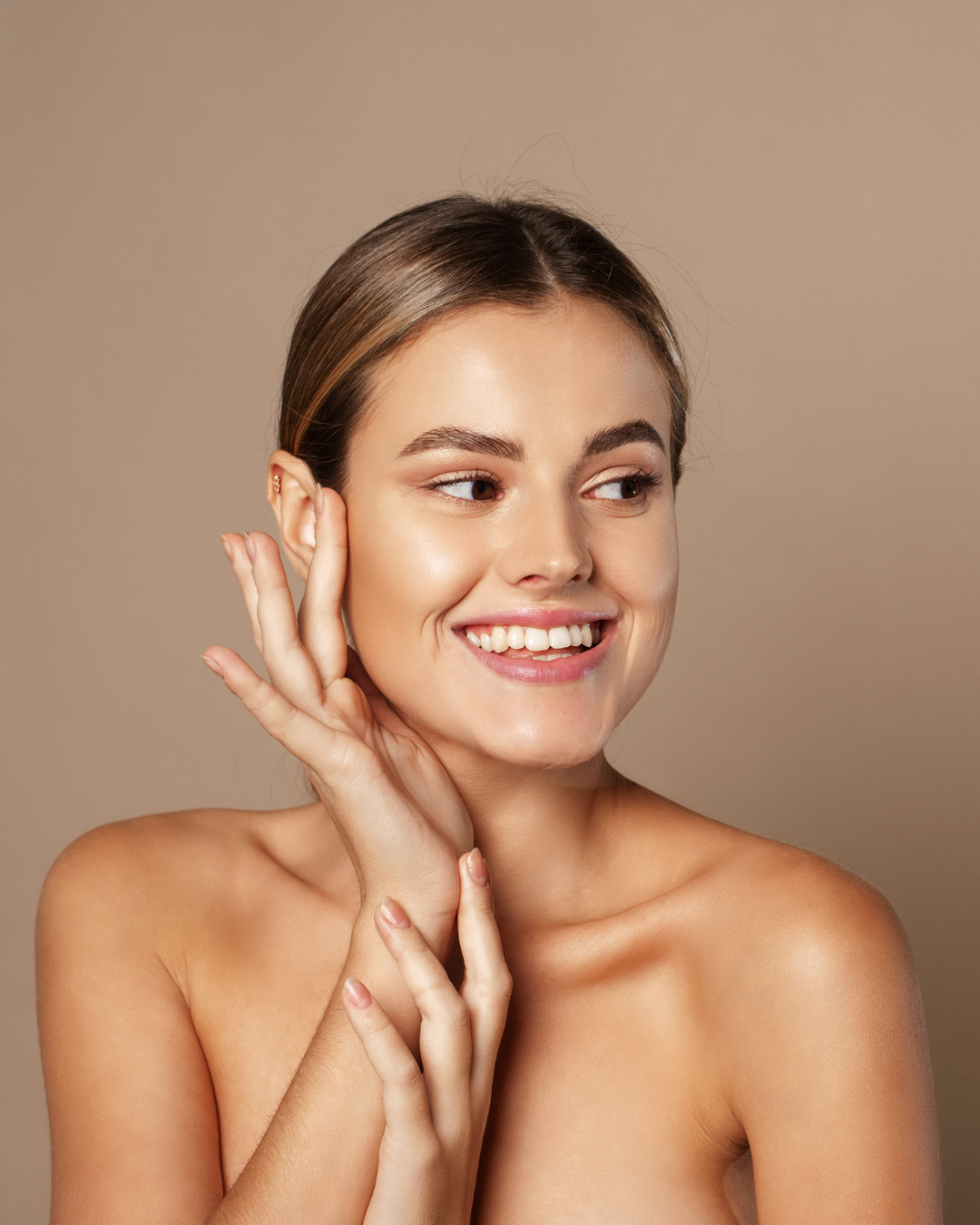 Woman with smooth skin touching her face against a beige background