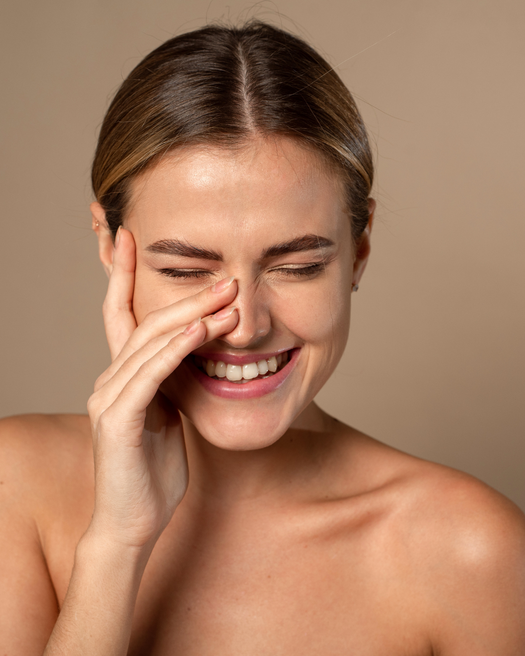 Woman with a bright smile touching her face against a beige background