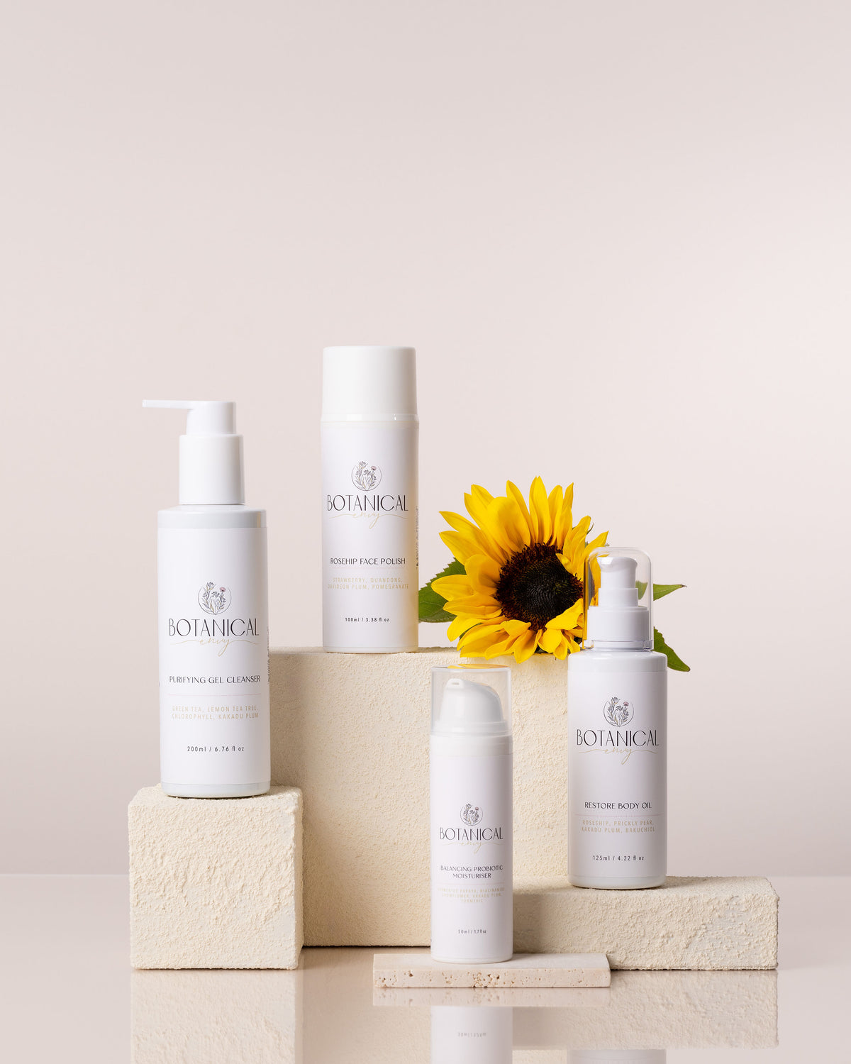A set of four white bottle skincare products sitting on top of stone bricks with a sunflower against a beige background 