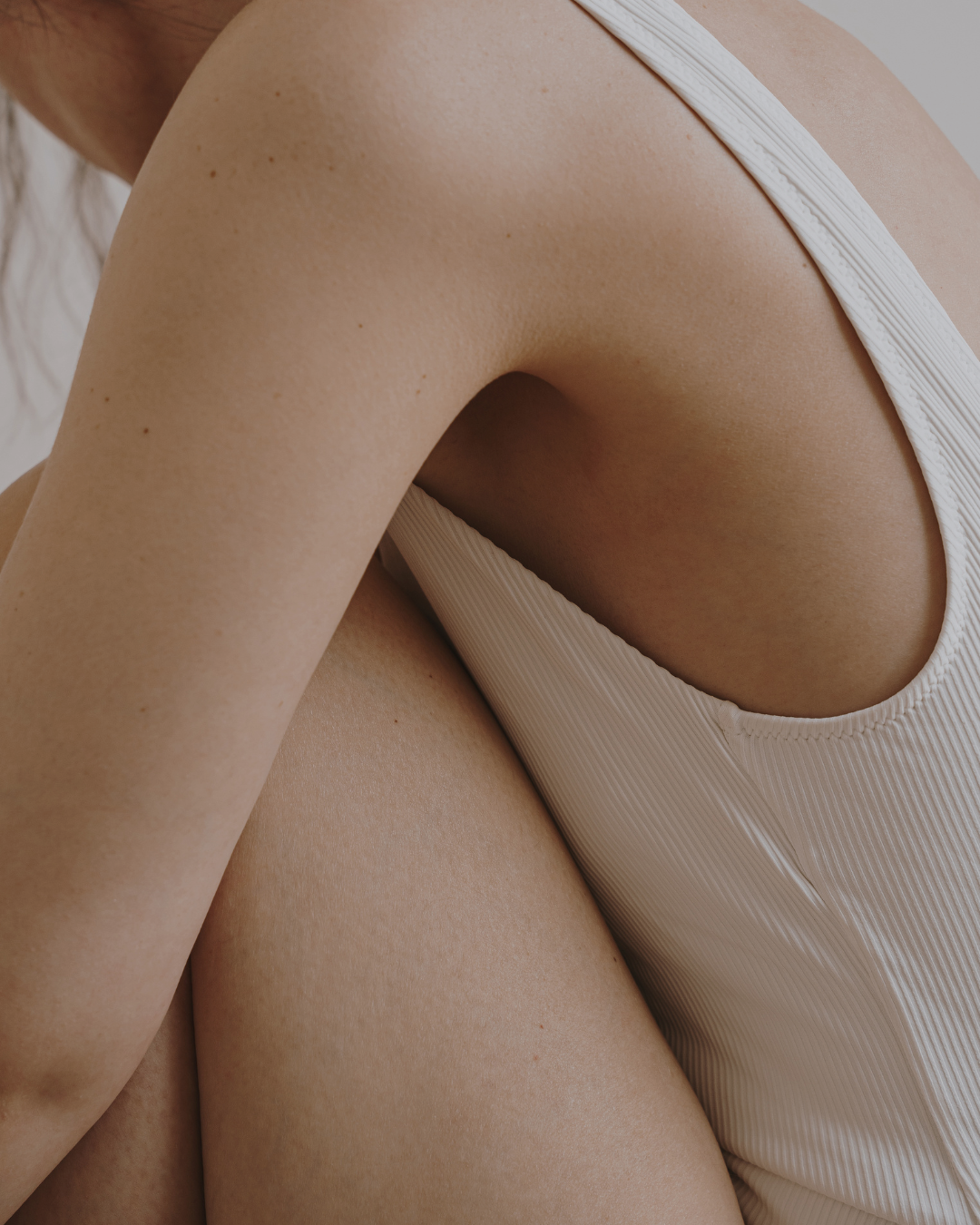 Close-up of a person wearing a ribbed cream-colored tank top, showing the back and shoulder area against a soft neutral background.