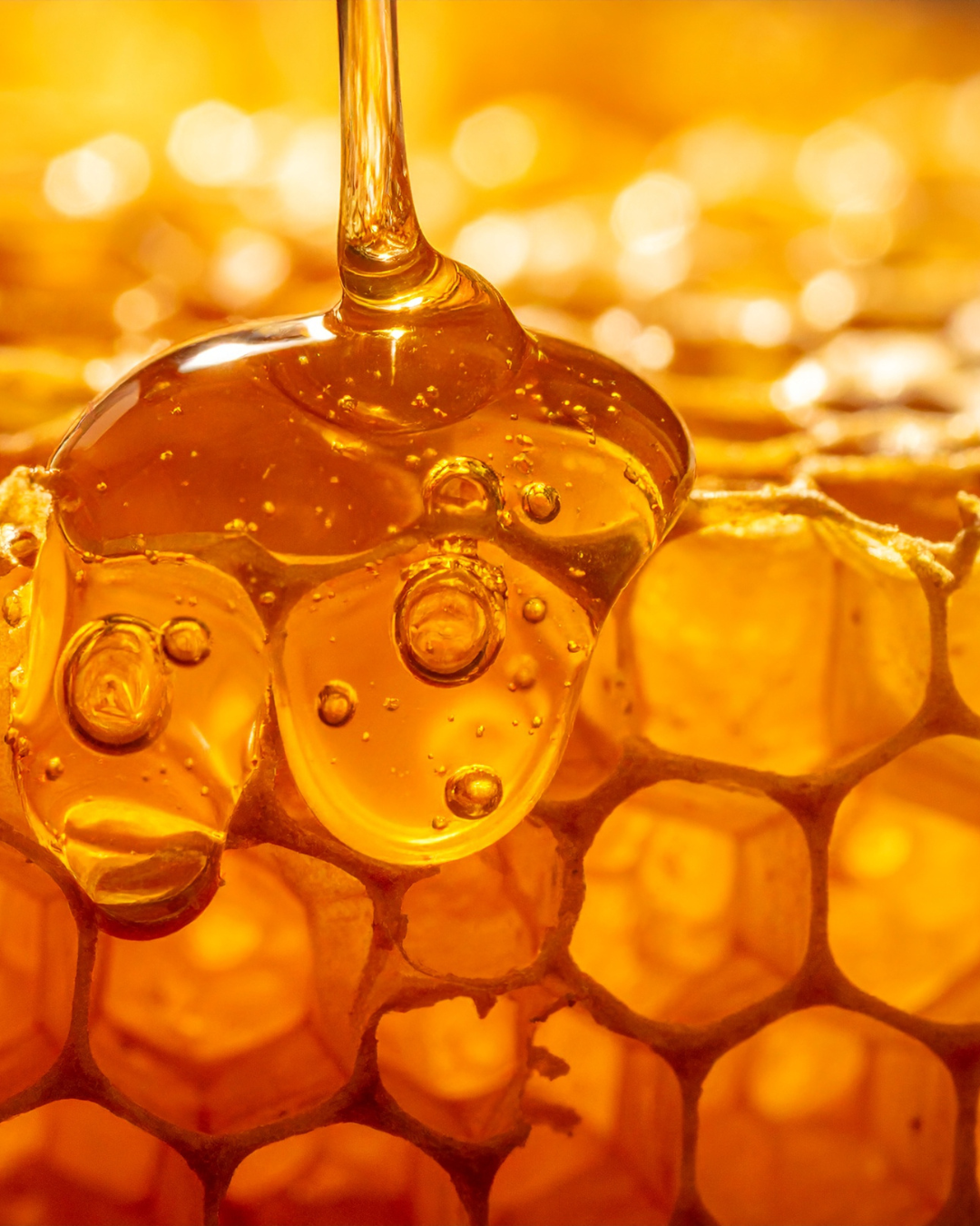 Honey being drizzled onto honeycomb with a blurred honeycomb background