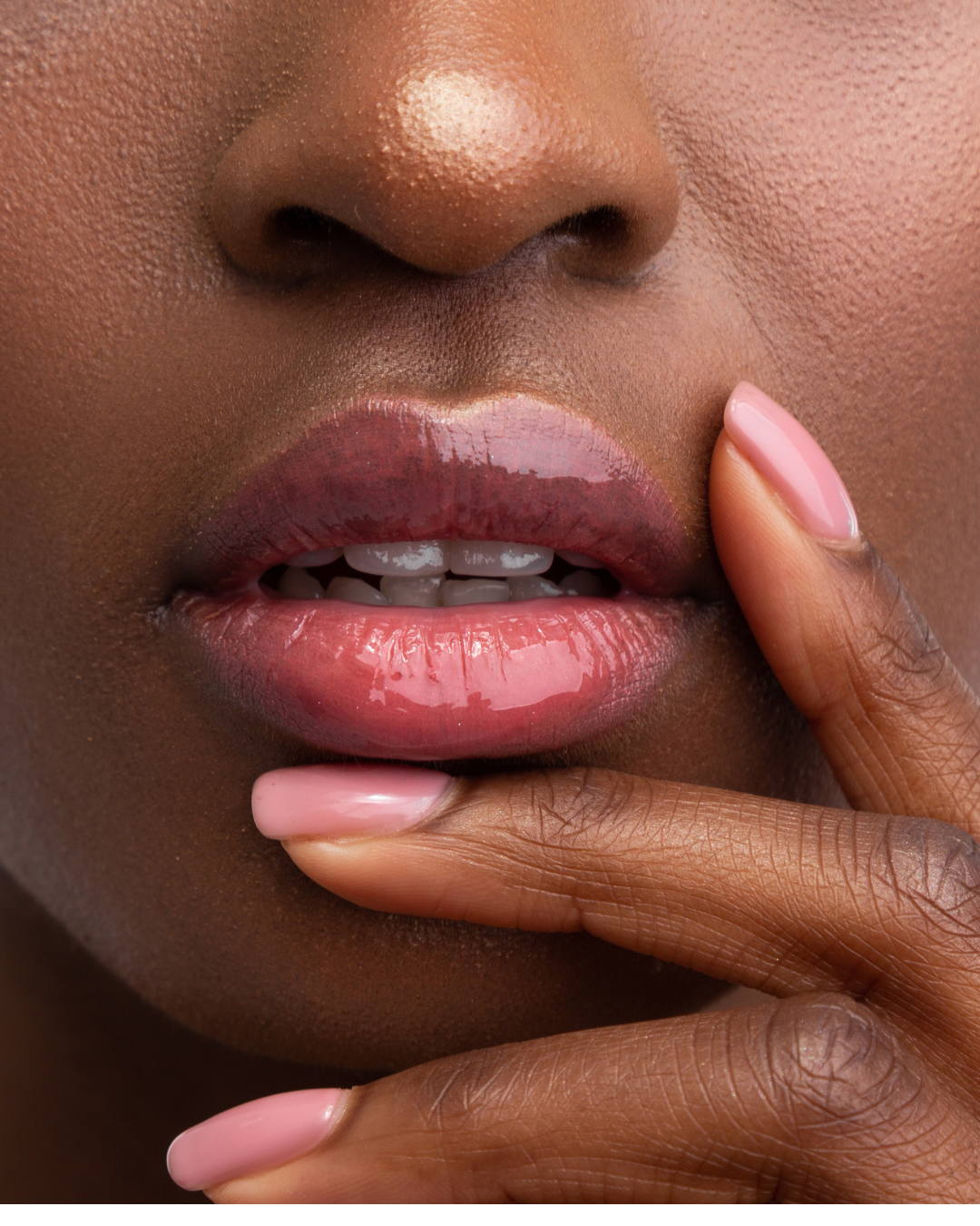 Close-up of glossy pink lips and manicured pink fingernails on a person's face.