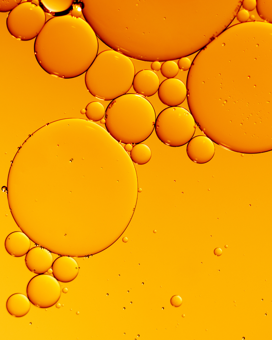 Abstract macro photograph of translucent golden-yellow oil droplets floating in a bright yellow-orange liquid.