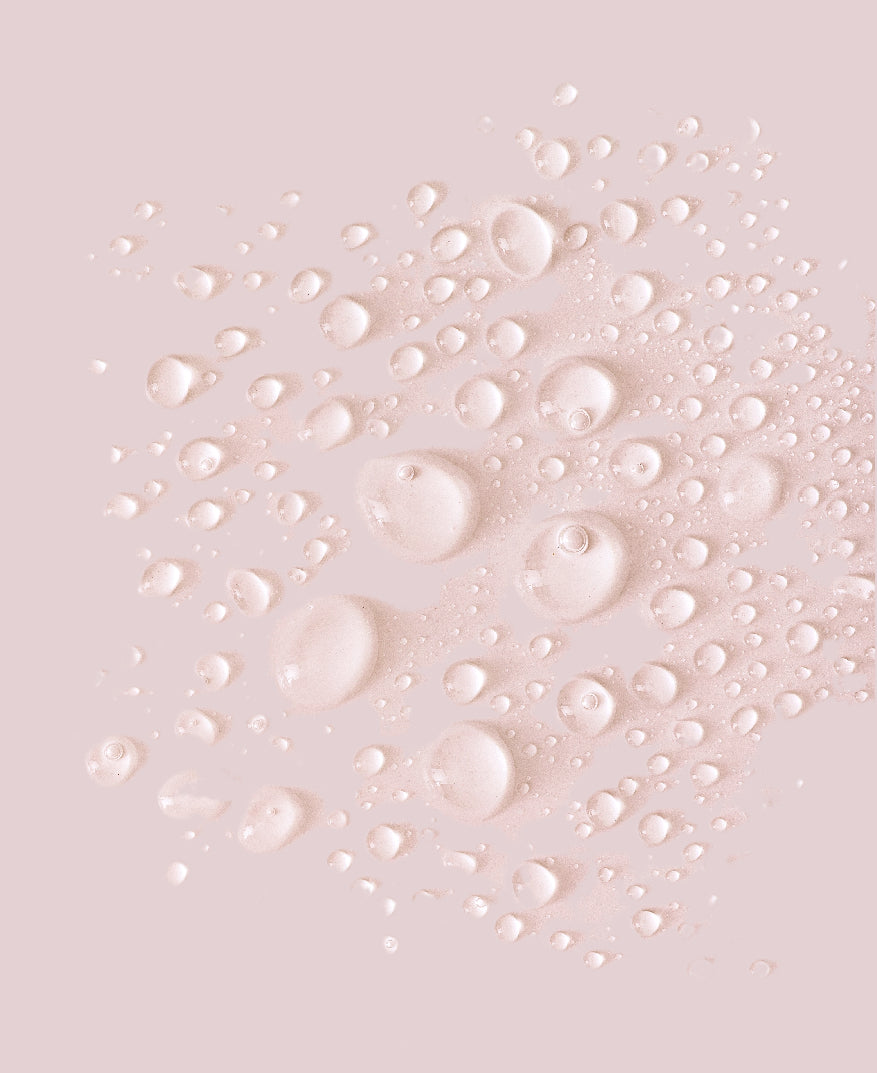 A close-up of translucent water droplets and bubbles on a soft blush pink background.